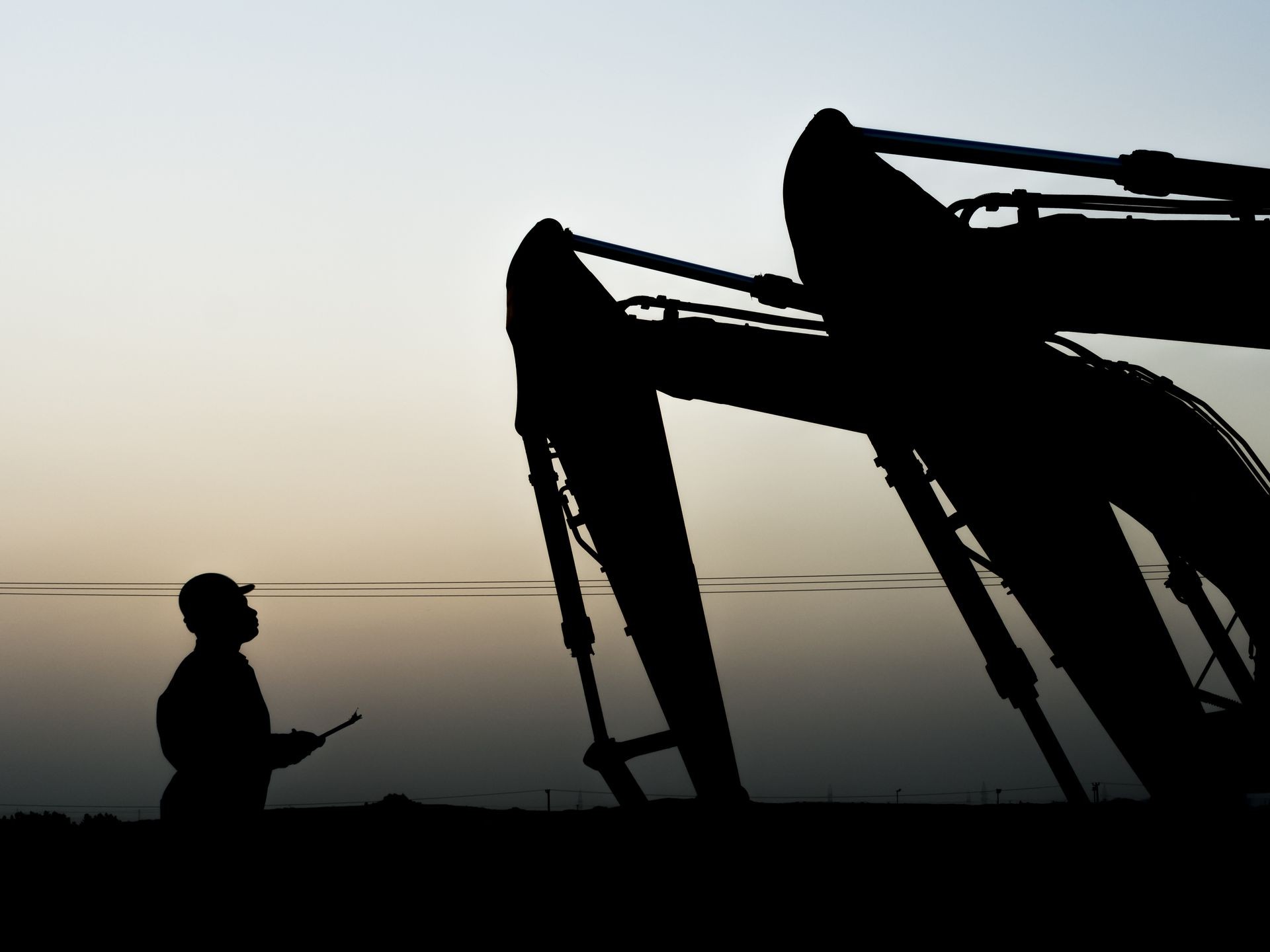Silhouette of oilfield worker inspecting the excavator in oilfield 